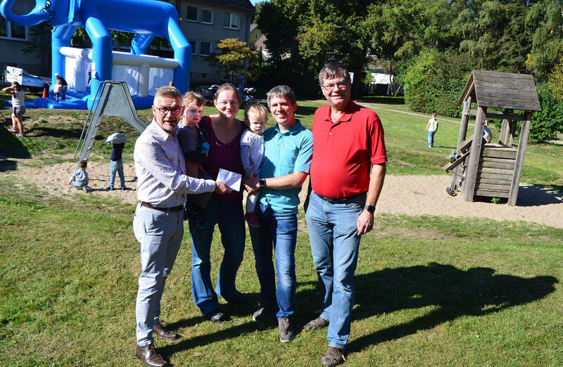 AWO-Chef Oliver Kern überreicht beim Spielplatzfest in Dellwig den Paten Vera und Torsten Hill eine Spende für neue Spielgeräte. SPD-Ratsherr Thomas Osterholt (1.v.r.) unterstützt die Aktion, Jonas (2.5) und Mara Sophie (1,5) freuen sich. Foto: AWO Essen/Grenz